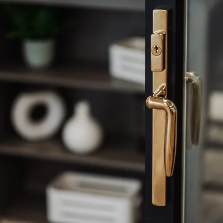 Close-up of a modern glass door with a gold handle and lock, blurred shelves in the background.