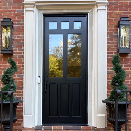 Black front door with glass panels on a red brick house with decorative topiaries and lanterns.