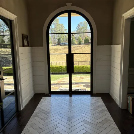 Elegant entryway showcasing arched glass doors and herringbone tile flooring with natural light.