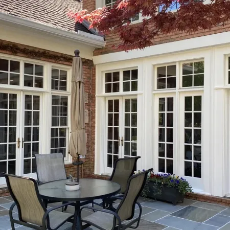 Outdoor patio with round table and chairs in front of multi-door glass windows on brick house