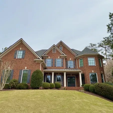 Spacious brick house with manicured lawns and symmetrical windows under a clear sky.