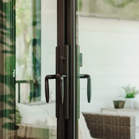 Close-up of dark metal door handles on glass sliding door leading to cozy wicker patio seating.