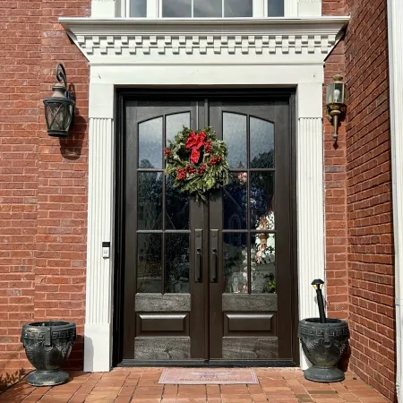 Black double front doors with glass panels and a Christmas wreath on a red brick house entrance.