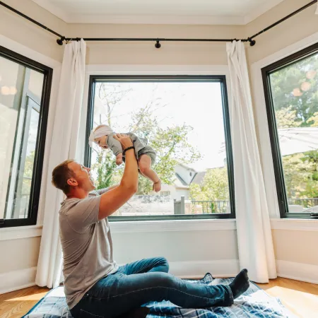 a person holding a baby in front of windows