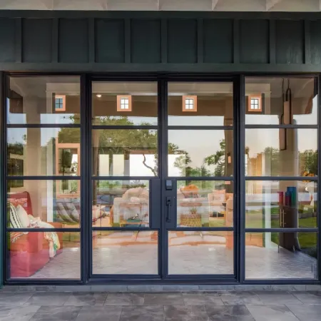 Modern black-framed glass double doors with outdoor wall lanterns leading to a spacious living room.