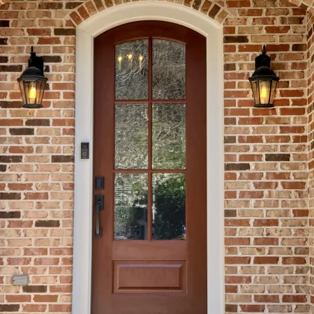 Brick house with arched entry door. Entry door is stained a dark wood tone with privacy glass.