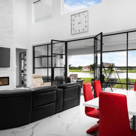 Modern living area with black leather sofa, red dining chairs, glass doors opening to lake view patio