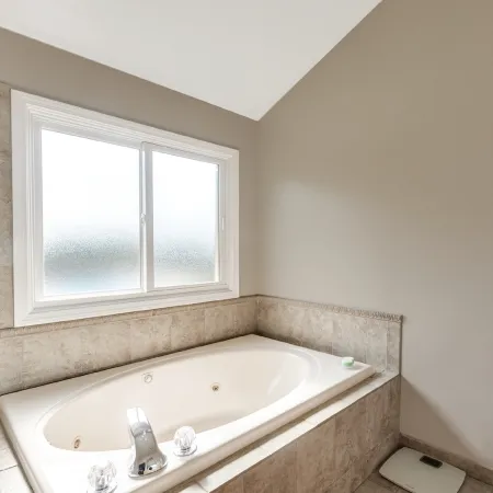 A bathroom with a soaking bathtub below a white slider window with privacy glass for easy ventilation.