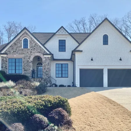 Modern two-story house with stone and white siding, double garage doors, American flag, and landscaped yard under clear sky
