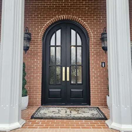 Arched black iron double entry doors with privacy glass on front porch of brick house