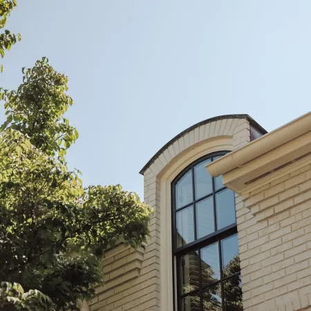 Arched black window on cream brick house with tree and clear sky in daylight