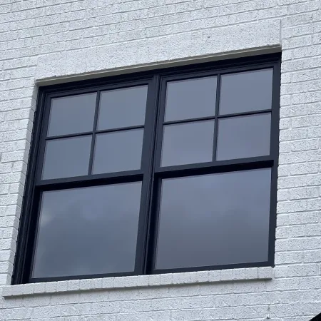 Two double hung fiberglass windows with black frames on white brick wall