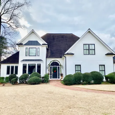 Elegant two-story white house with lush greenery and black fiberglass replacement windows