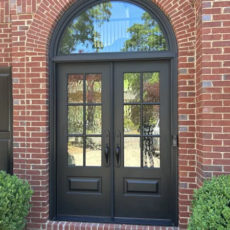 Elegant black double doors with arched glass, framed by red brick and lush greenery.