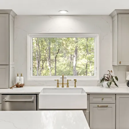 Modern kitchen with a large white awning window overlooking trees.