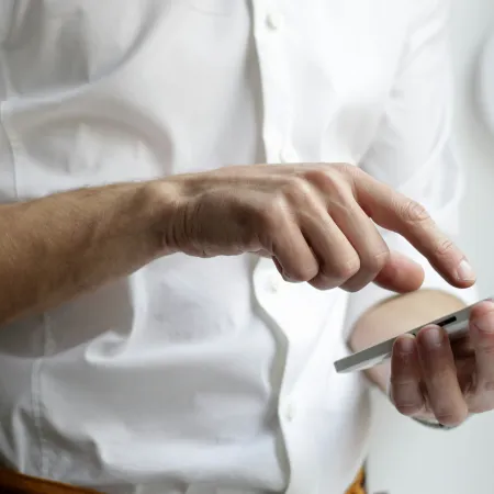 Person wearing white shirt using smartphone with one hand tapping on the screen.