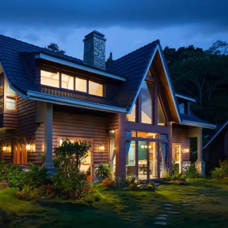 Cozy modern wooden house with glowing windows at dusk surrounded by greenery and garden lights