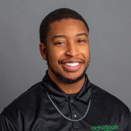 Smiling young man wearing a black OrthoSouth polo shirt with a silver chain necklace on gray background