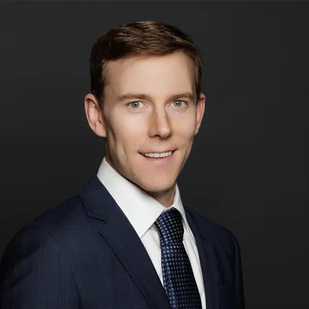 Professional young man with light eyes wearing a dark blue suit and patterned tie smiling against black background