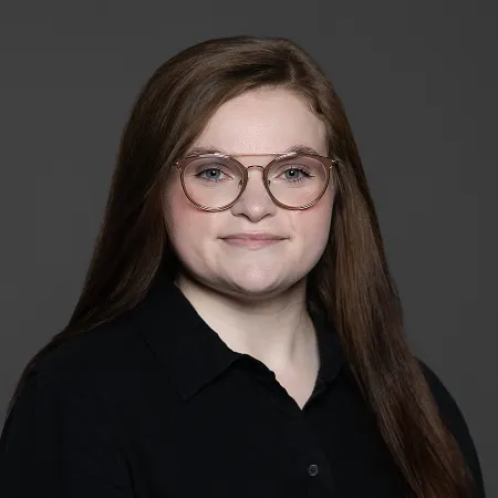 Portrait of a smiling woman with long brown hair wearing glasses and a black shirt against a dark background