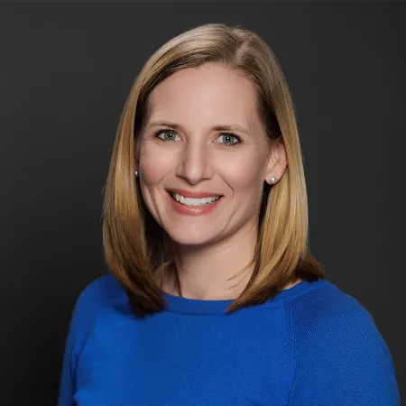 Smiling woman with blonde hair wearing a blue sweater against a dark background portrait