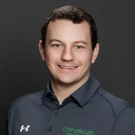 Smiling man wearing a dark OrthoSouth branded polo shirt on a plain dark background.