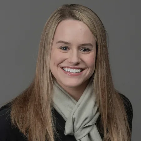 Portrait of smiling woman with long blonde hair wearing a light scarf and dark top against gray background