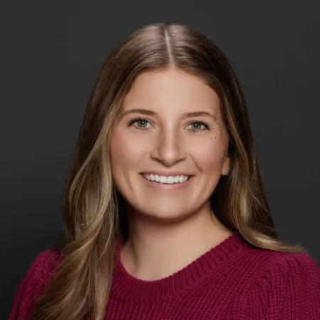 Smiling woman with long blonde hair wearing a maroon sweater against a dark grey background.