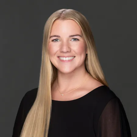 Smiling woman with long blonde hair wearing a black top against a dark gray background