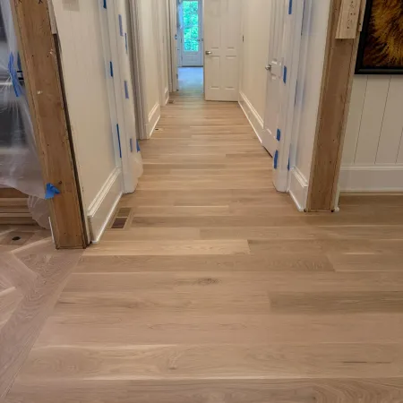 Newly installed light wood flooring in a bright hallway with white walls and open doors at the end.