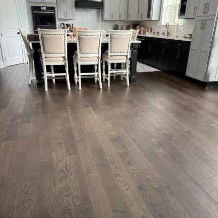 Modern kitchen with dark hardwood floors, white and black cabinets, and beige upholstered chairs at island.