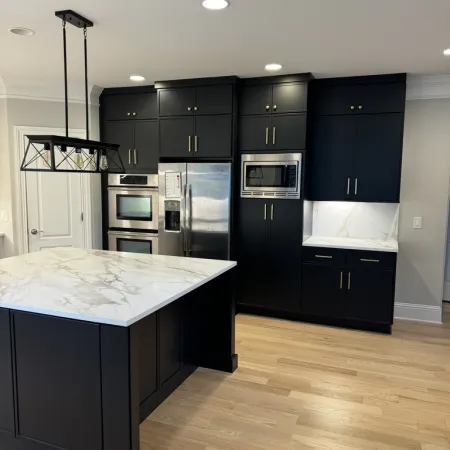 Modern kitchen with black cabinetry, marble countertops, stainless steel appliances, and light wood flooring.