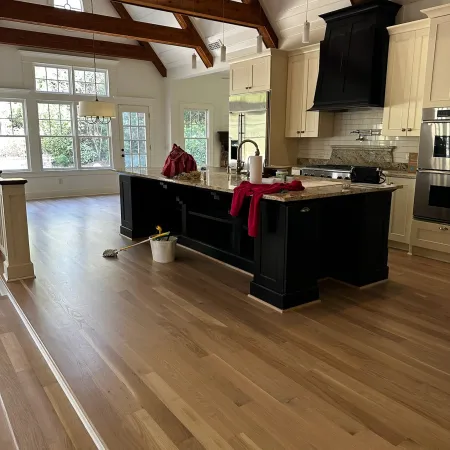 Spacious modern kitchen with hardwood floors, exposed wooden beams, large island, and natural light from windows.
