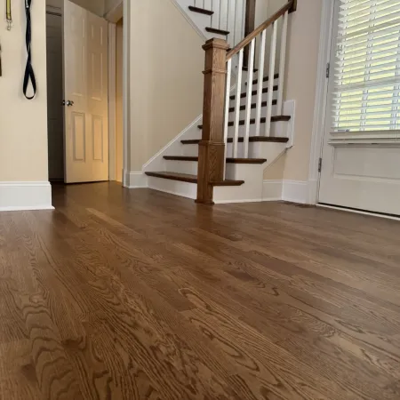 Smooth wooden flooring in a home entryway featuring a staircase, door, and wall hooks with straps.
