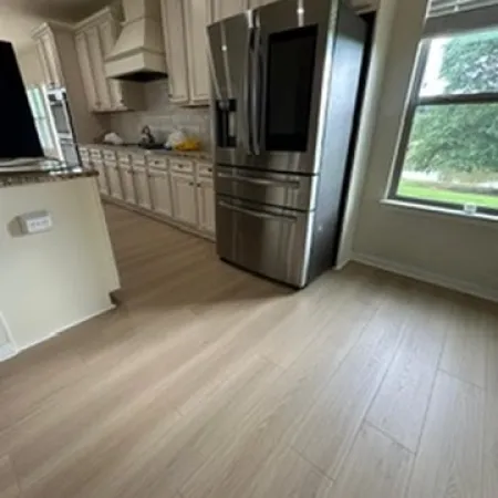 Modern kitchen with stainless steel refrigerator, white cabinets, hardwood floors, and large window with natural light.