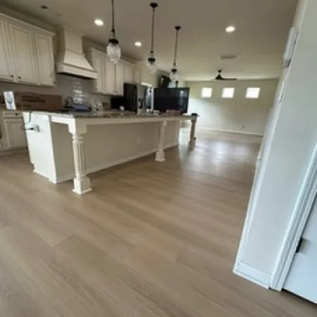 Spacious modern kitchen with light wood flooring, white cabinetry, large island, and pendant lighting.