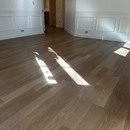 Sunlight streaming onto polished wooden floors in a bright, empty room with white paneled walls.