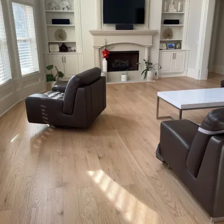 Bright living room with light hardwood floors, dark leather chairs, white fireplace, and built-in shelves.
