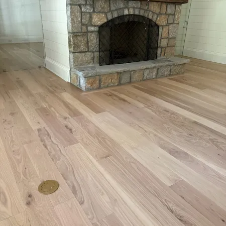Stone fireplace with wooden mantel and light hardwood floor in modern room with white walls.