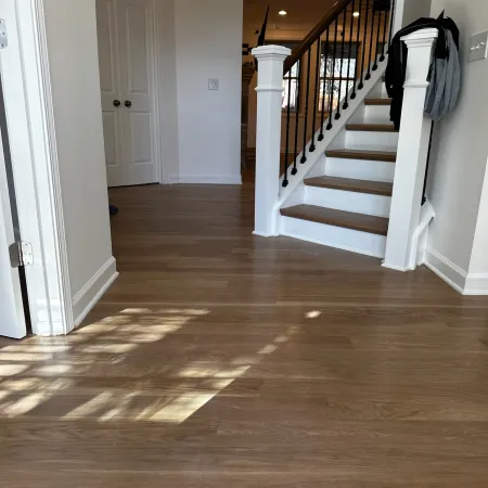 Bright entryway with wooden flooring, white walls, and staircase with black iron balusters under soft lighting.