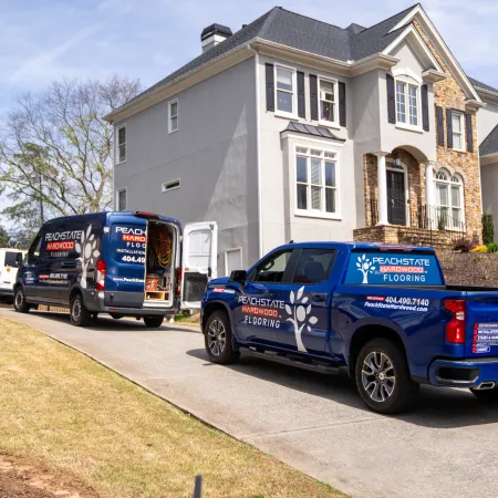 Peachstate Hardwood Flooring trucks parked outside a two-story suburban house on a sunny day.