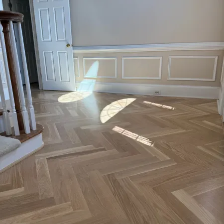 Sunlight casts window-shaped patterns on a light herringbone wood floor in an empty room with white paneled walls and an open door.