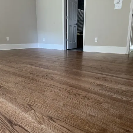 Empty room with newly installed medium brown hardwood flooring and beige walls with white baseboards.