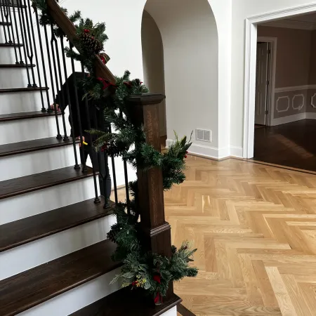 Wooden staircase with dark steps decorated with green garland and pine cones in a modern home with hardwood floors.