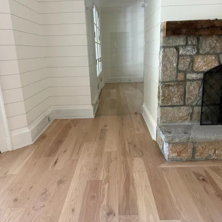 Light wood flooring leading to glass door with white shiplap walls and rustic stone fireplace.