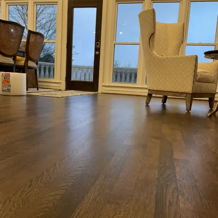 Wooden floor with armchairs and large windows showing outdoor balcony and trees in background
