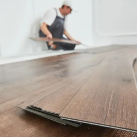 Worker installing dark wood laminate flooring panels in a bright room with white walls.
