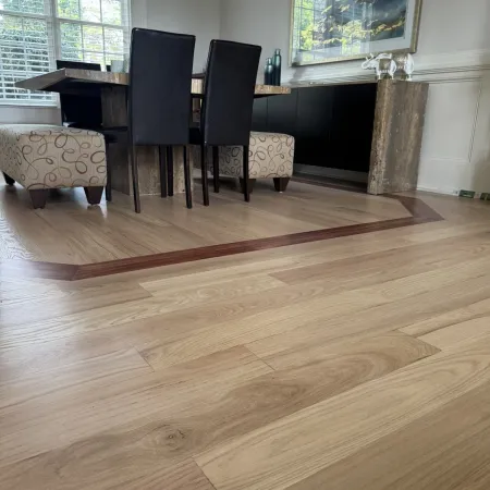 Modern dining room with light wood floor featuring a darker wood border, black chairs, and patterned benches.