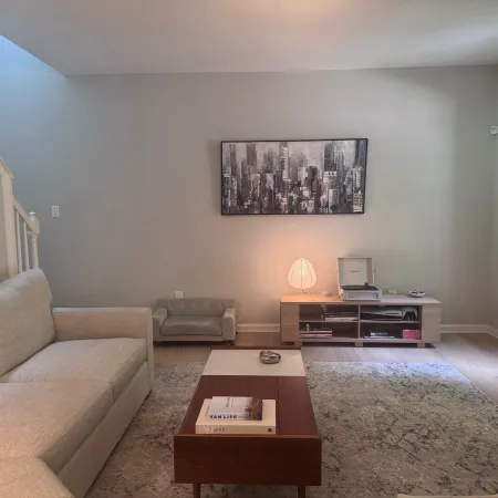 Bright living room with beige sofa, modern coffee table, rug, media console, and cityscape wall art under soft lighting.