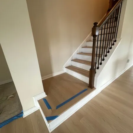 Newly installed light wood flooring and stairs with blue painter's tape outlining edges in a home interior.